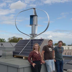 Zwei Männer und eine Frau stehen auf dem Dach eines Hauses vor einem Wind-Solar-Kleinkraftwerk.