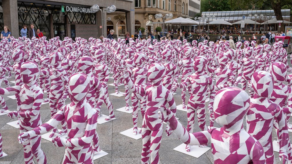 333 Kinderfiguren in purpur-weißem Flatterband vor dem Kölner Dom