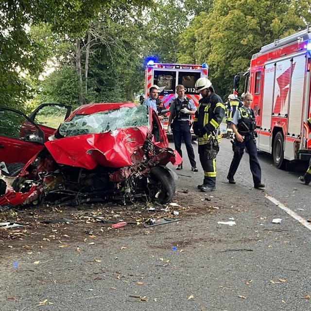 Schwerer Unfall in Köln-Worringen: Feuerwehrleute und Polizistinnen und Polizisten stehen am Dienstagbaend an dem extrem beschädigten Autowrack auf der Neusser Landstraße.