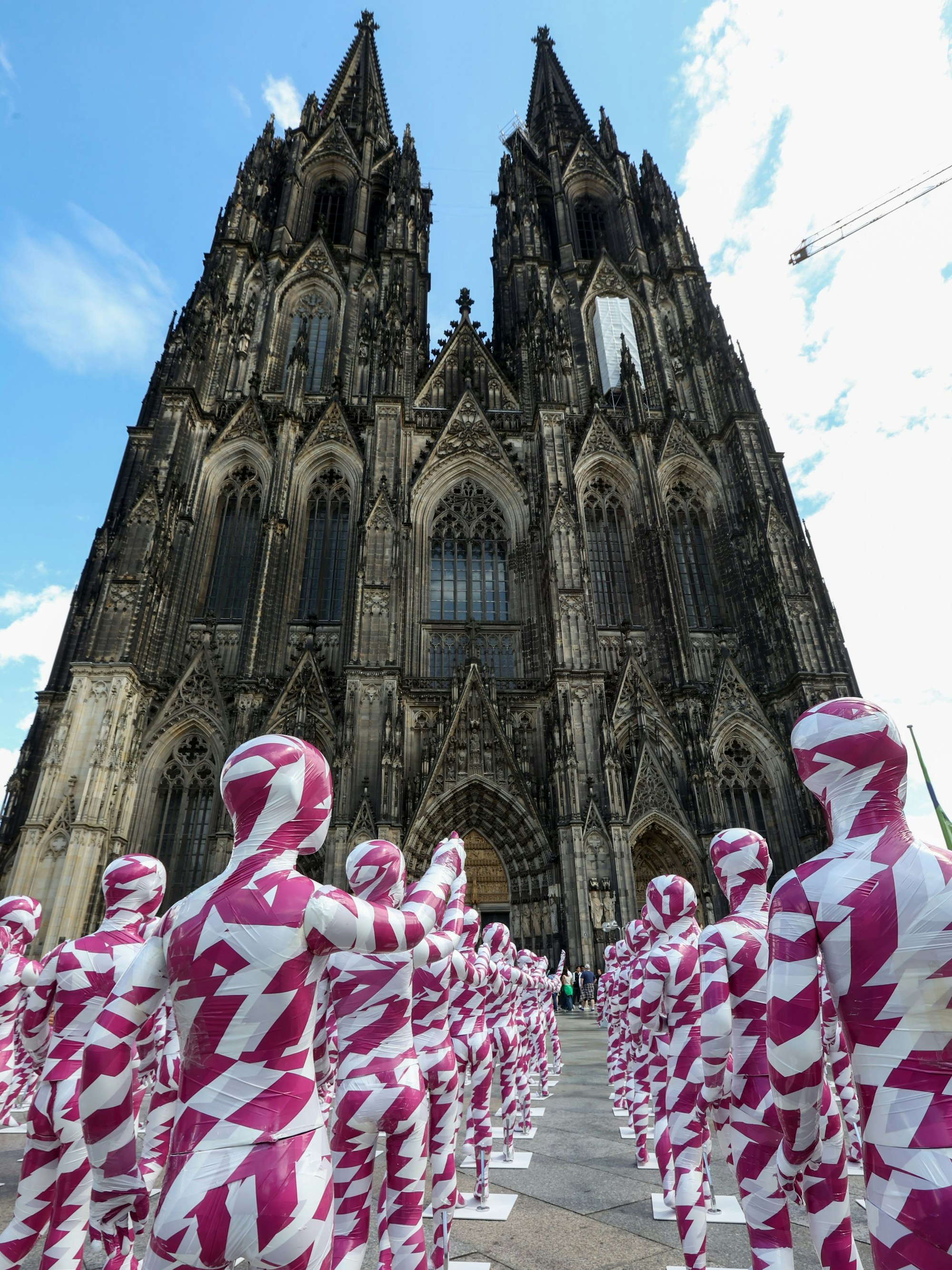 333 Kinderfiguren stehen als Mahnwache vor dem Kölner Dom. Die mit purpur-weiß farbigem Flatterband umhüllten Figuren zeigen mit dem Finger auf den Dom.