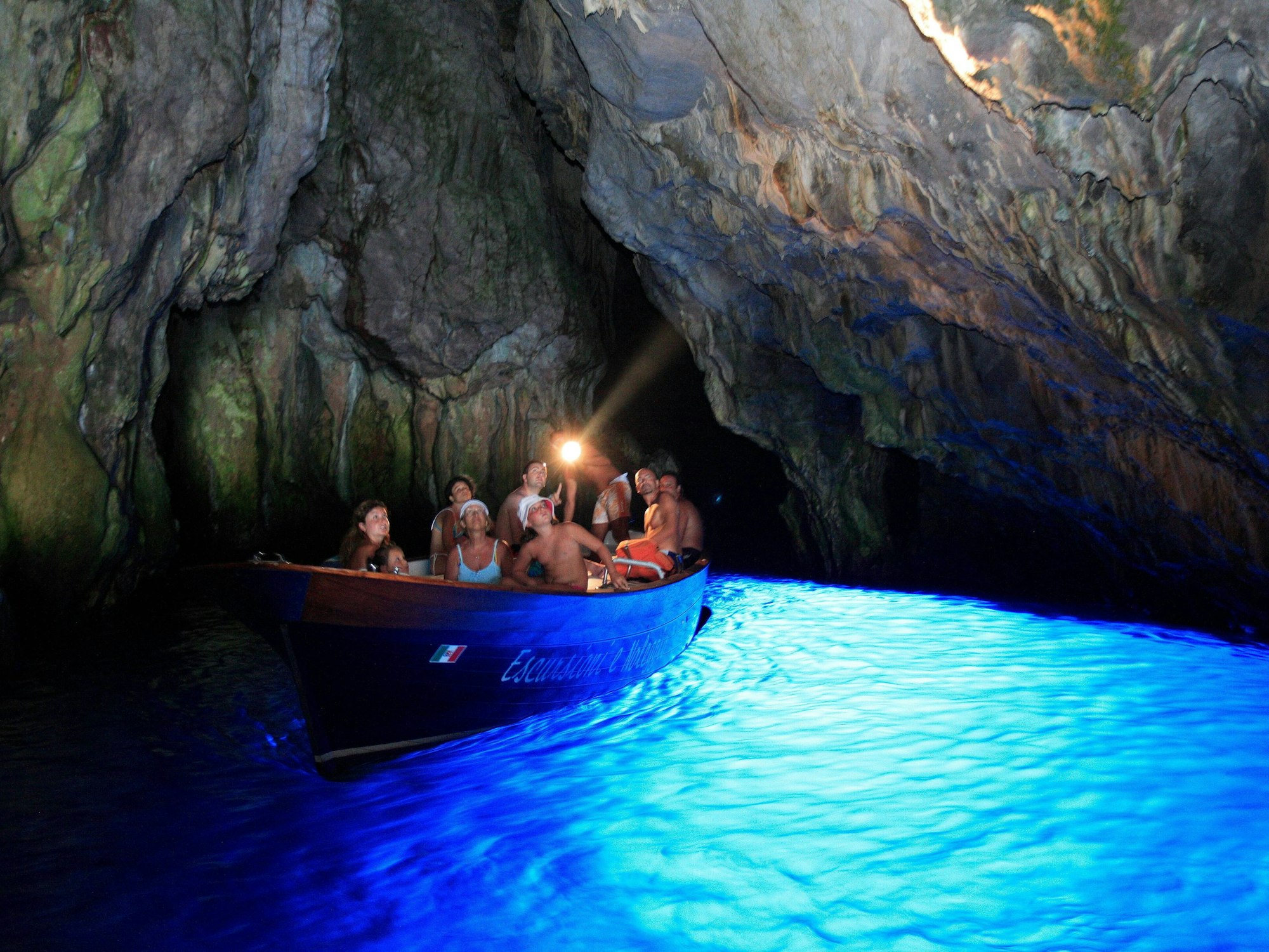 Ein Boot mit mehreren Personen fährt durch das blaue Wasser in der Höhle (März 2021).