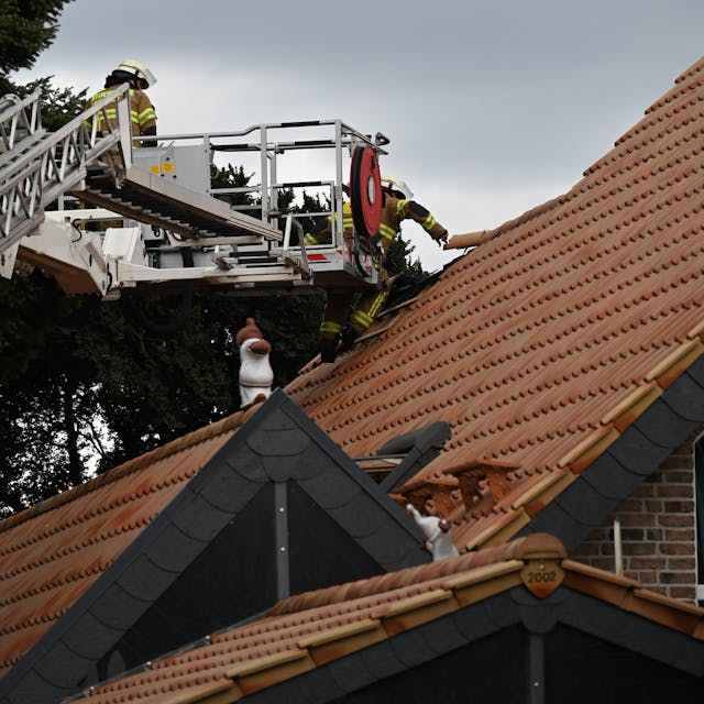 Das Bild zeigt Feuerwehrleute an einem Hausdach, die die Ziegel entfernen.