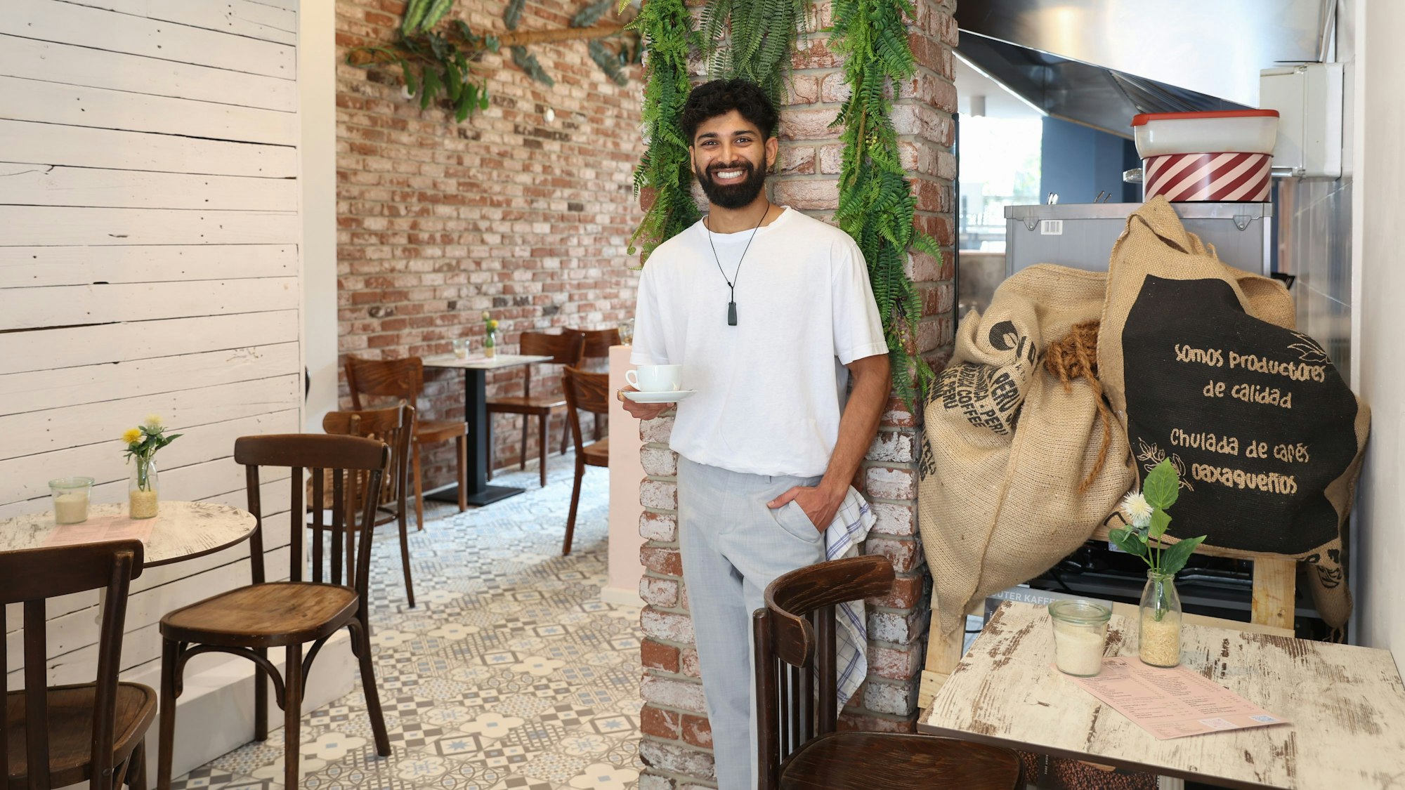 Kassim Hussain steht an einer Säule und hält eine Tasse Kaffee.