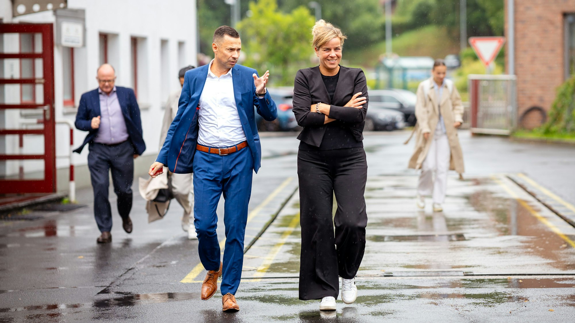 Ein Mann und eine Frau gehen über eine regennasse Straße auf dem Werksgelände der Firma Schoeller in Hellenthal.