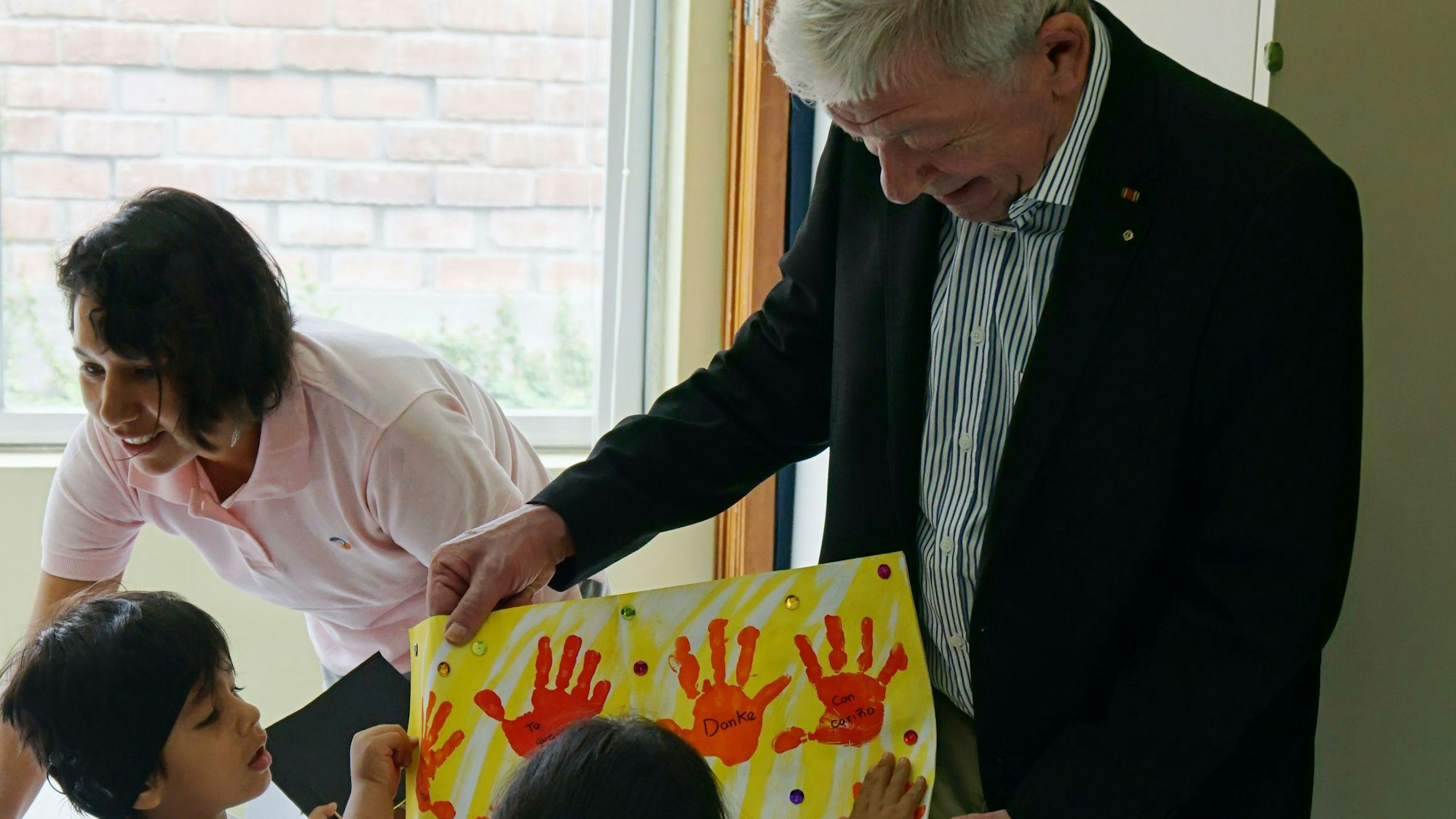 Manfred Görgens betrachtet ein Bild mit gelbem Hintergrund und roten Handabdrücken, das ihm Kinder zeigen.