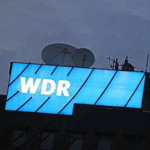 Das Logo des Nachrichtensenders WDR leuchtet auf dem Dach des WDR-Gebäudes in der Kölner Innenstadt.