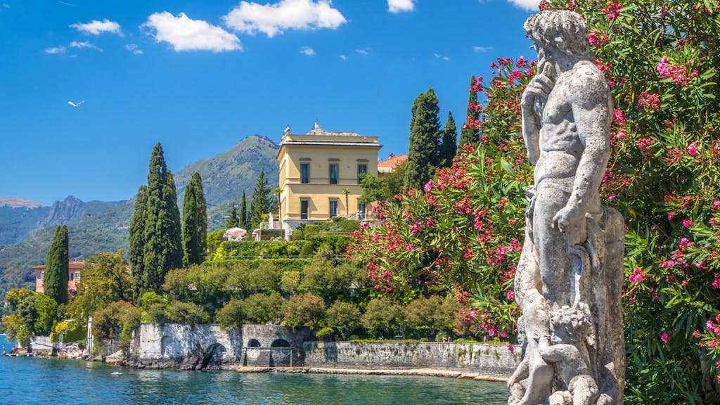 Eine Statue steht am Wasser des Sees. Im Hintergrund steht eine Villa.
