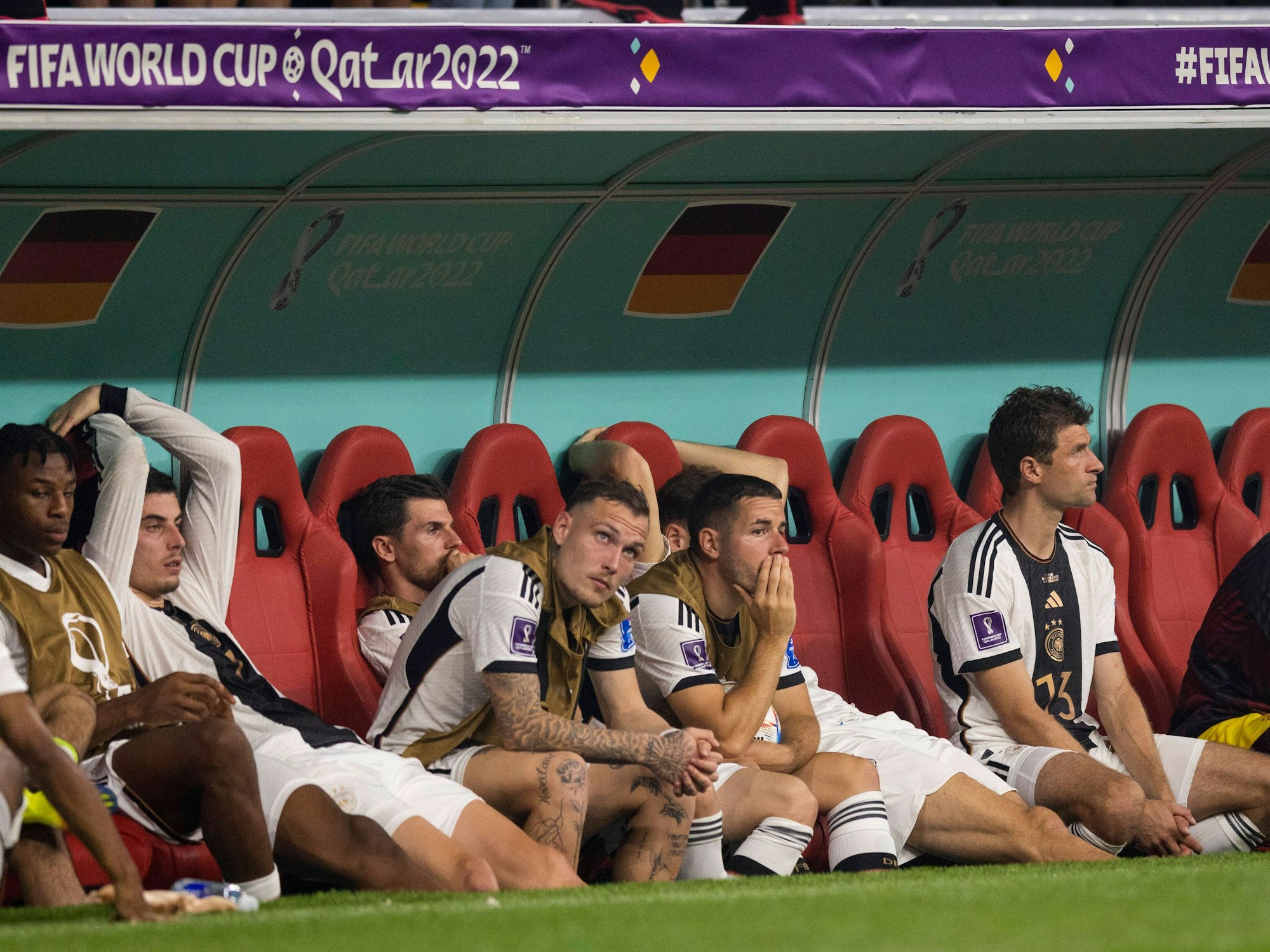 Die Nationalspieler Thomas Müller, Kai Havertz und David raum sitzen niedergeschlagen auf der Ersatzbank. 