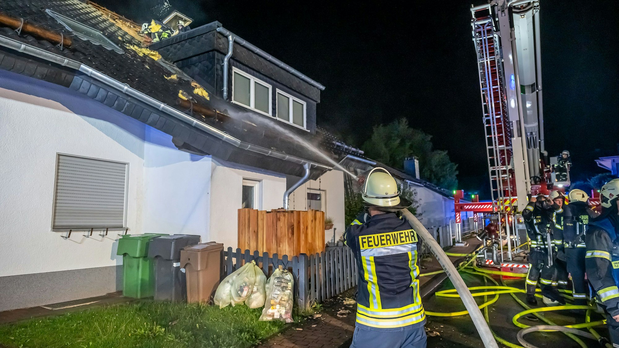 Ein Feuerwehrmann hält einen Schlauch, aus dem ein Wasserstrahl kommt, in Richtung eines brennenden Dachstuhls.
