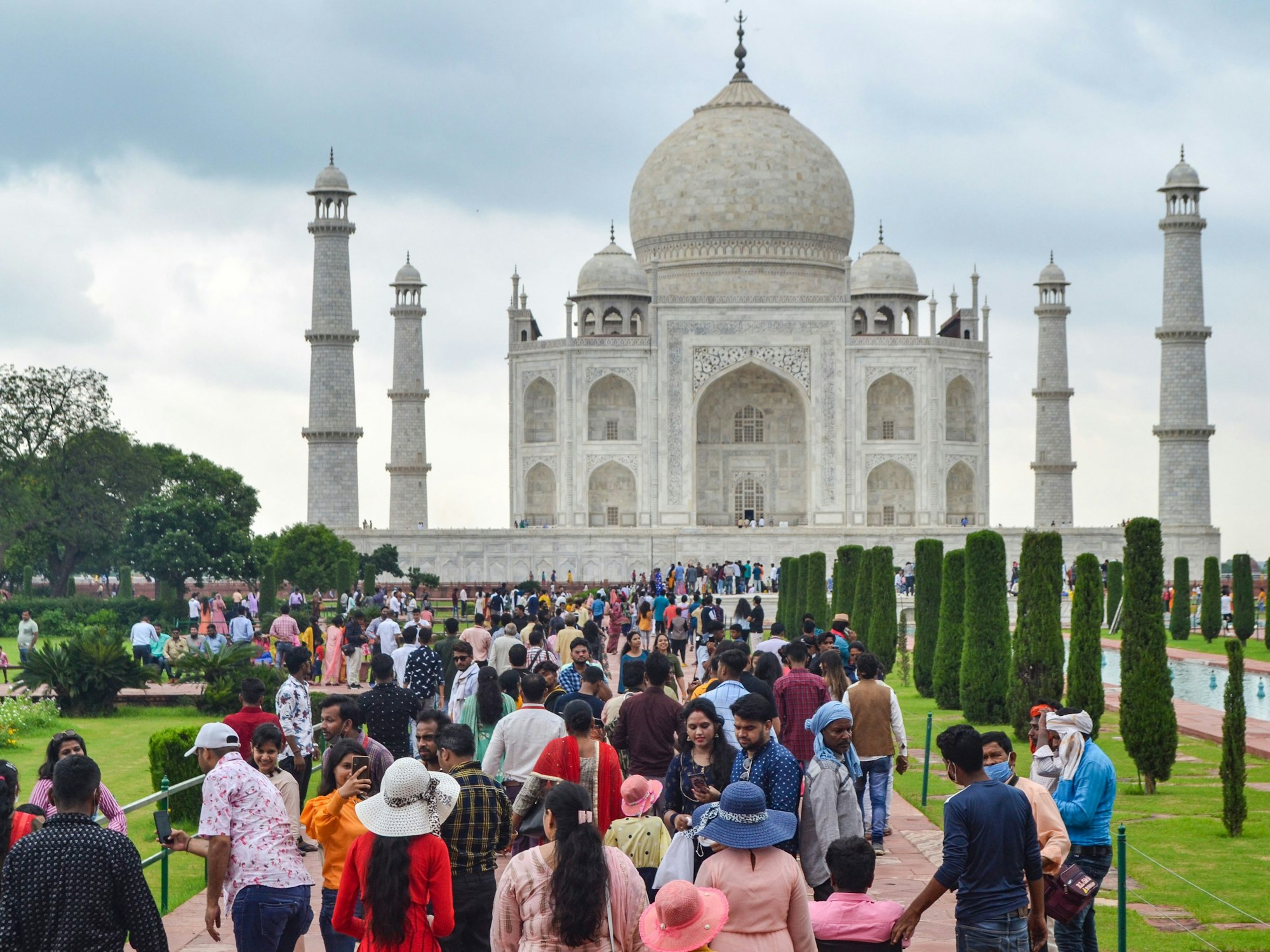 Touristinnen und Touristen besuchen an einem bewölkten Tag den Taj Mahal.