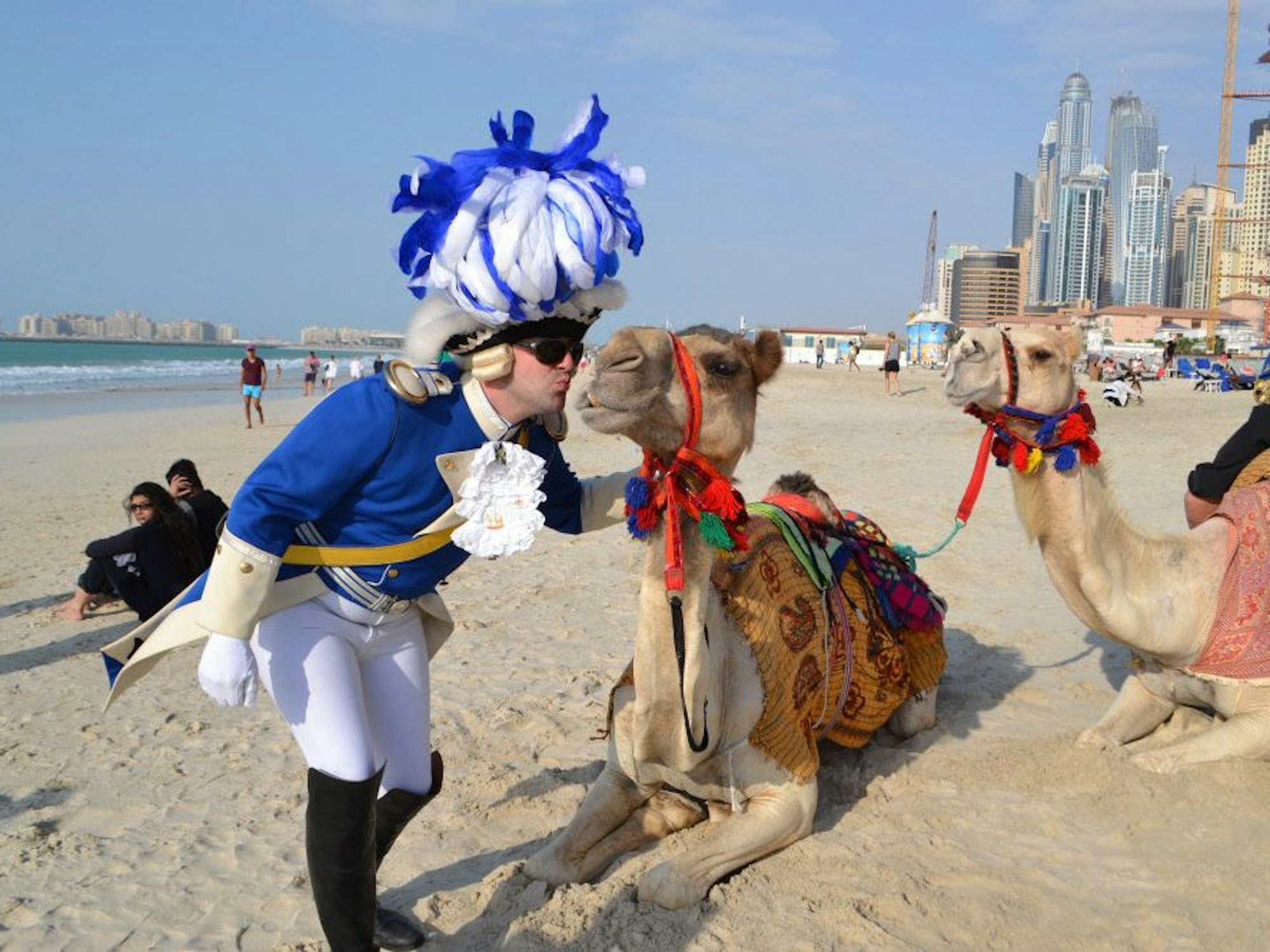 Ein kostümierter Karnevalist küsst ein Kamel an einem Strand