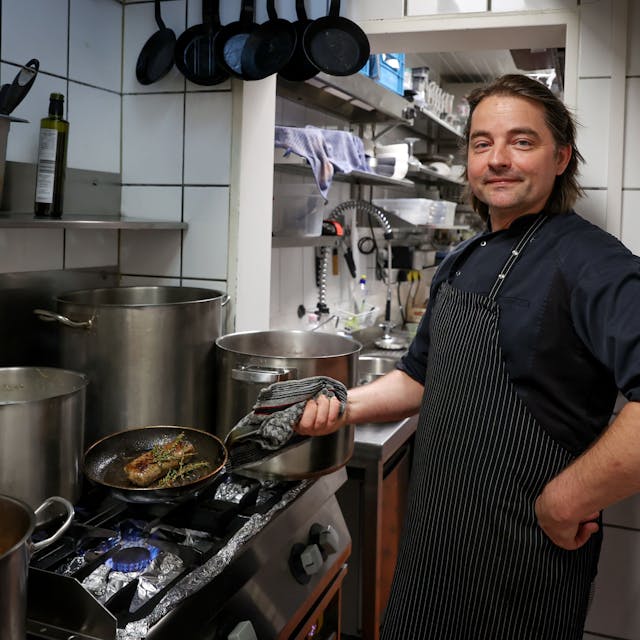 David Safanda vom Crevette Rosé steht in der Küche und brät ein Stück Fleisch in der Pfanne.