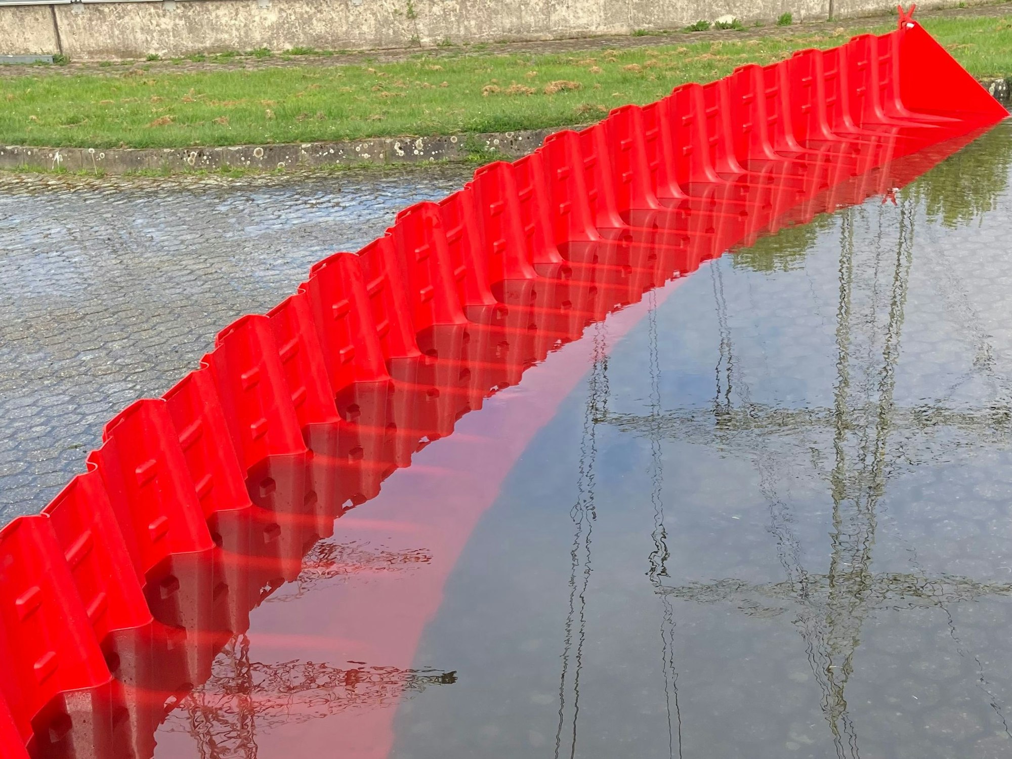 Rote Kunststoff-Elemente bilden zusammengesteckt eine kleine Mauer, die Wasser auf einer Straße zurückhält.