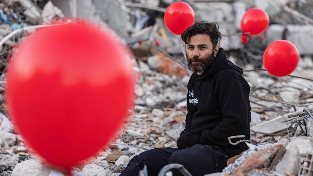 Ogun Sever Okur, ein 38-jähriger Türke, zwischen Luftballons, die an den Trümmern eines eingestürzten Gebäudes in Antakya in der Südtürkei hängen. Vielen Menschen im Erdbebengebiet droht nun die nächste Katastrophe.