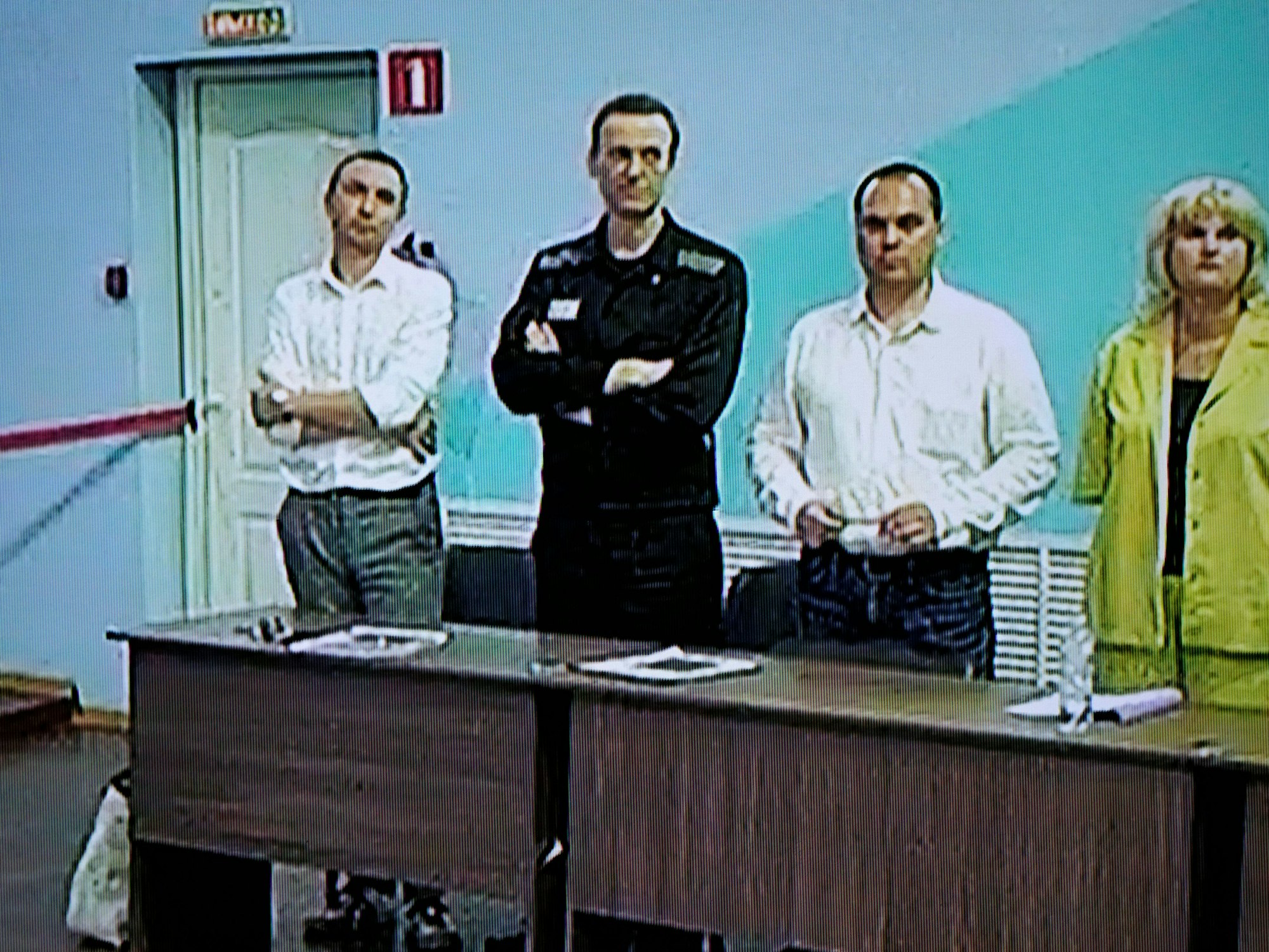 Alexej Nawalny (2.v.l) ist in einem von der russischen Strafvollzugsbehörde zur Verfügung gestellten Videolink auf einem Bildschirm zu sehen, während er bei einer Anhörung neben seinen Anwälten steht.