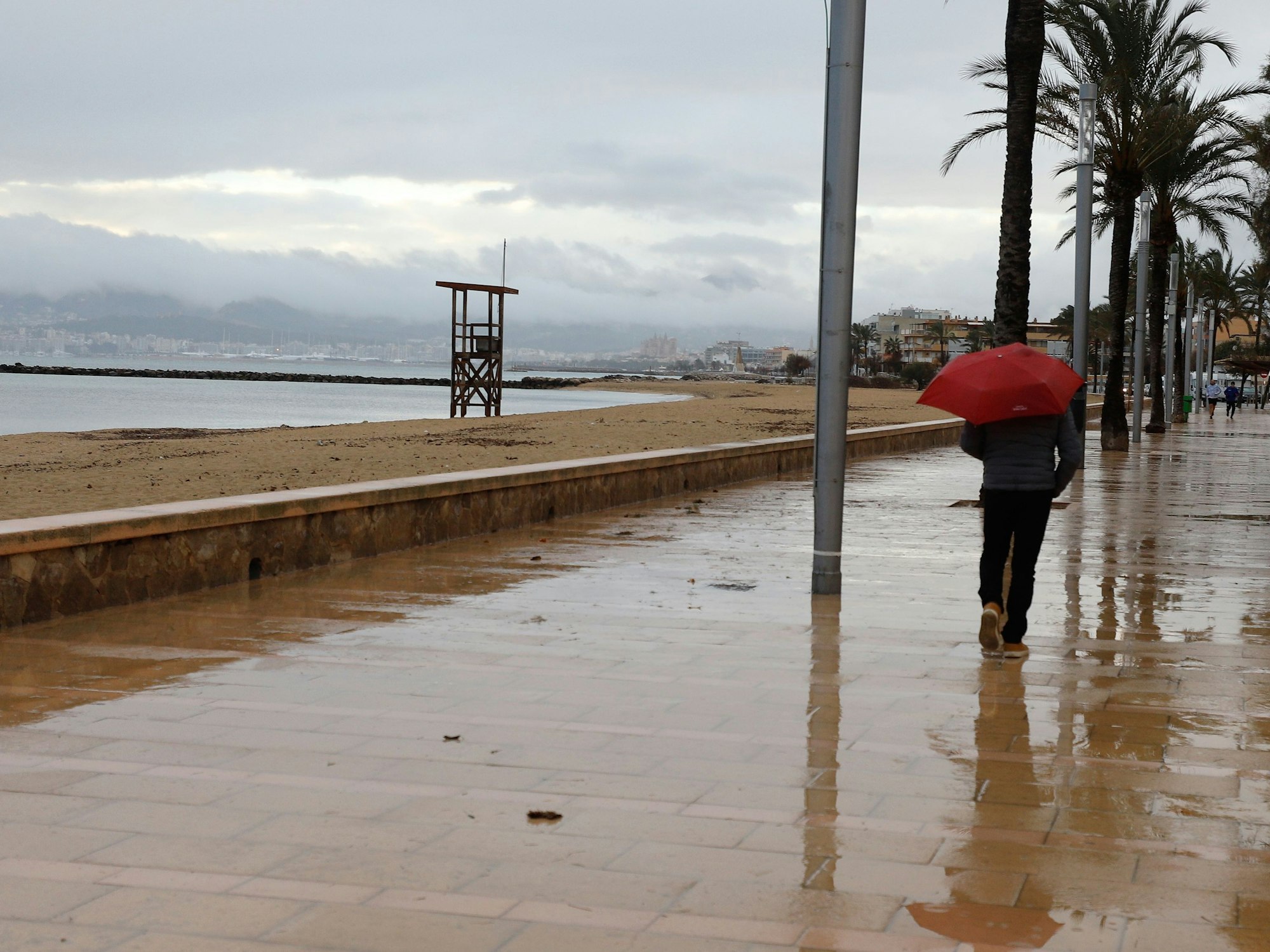 Ein Mann spaziert mit einem Regenschirm am Strand von Palma entlang, hier im Dezember 2020.