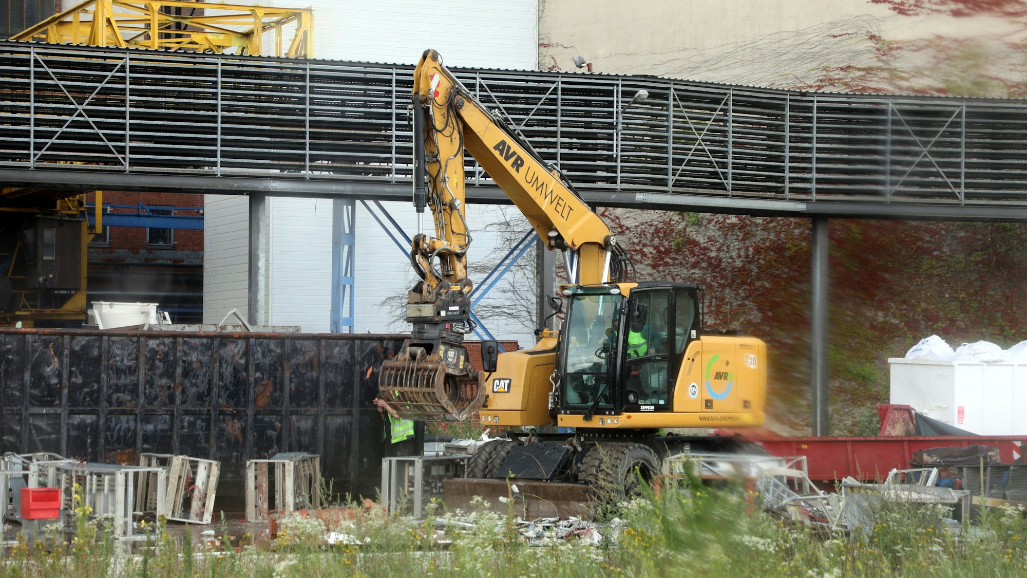 Ein Bagger greif Metallteile vor einem Werksgebäude.