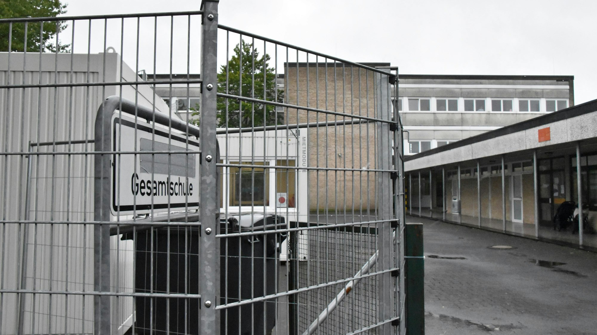 Hinter einem Zaun steht das Schild Gesamtschule. Es weist auf den Haupteingang des Standorts Rosbach hin.