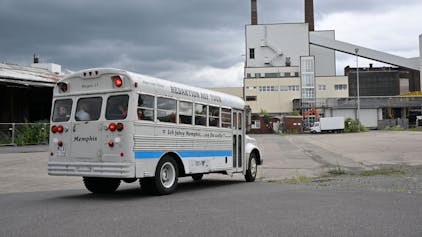 Ein historischer amerikanischer Schulbus mit der Aufschrift „Redaktion auf Tour“ fährt über das Bergisch Gladbacher Zanders-Gelände auf das dortige Kraftwerk mit Schornsteinen zu,