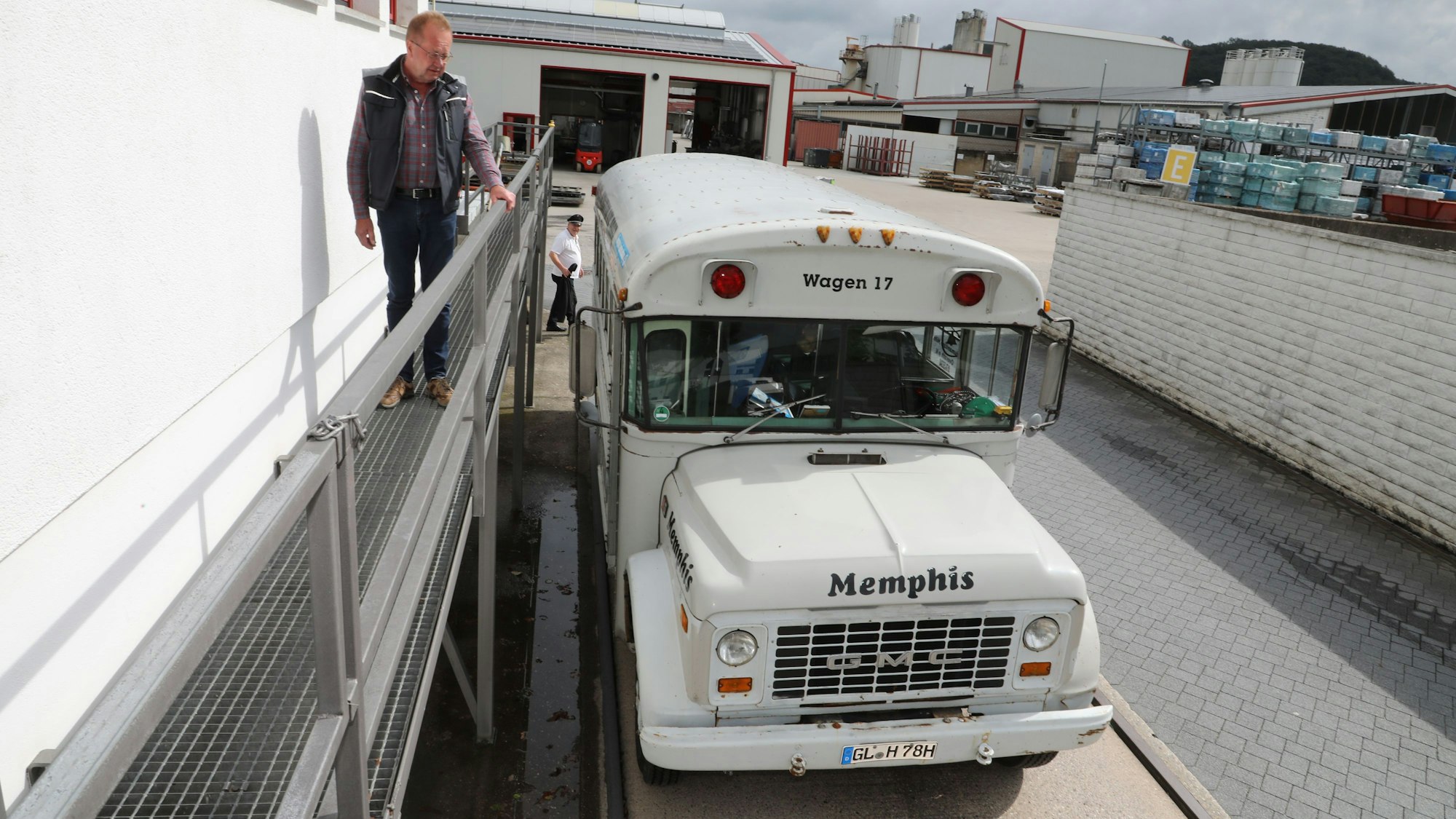 Ein Mann steht auf einem Gittergang und schaut zu einem historischen Bus, der auf einer Lkw-Waage darunter steht.