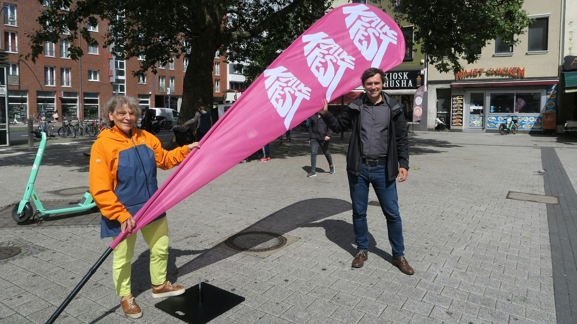 Maria Schweizer-May und Alexander Tschechowski zeigen eine Beach-Flag mit der Aufschrift „Kalk Fest“ an der Kalker Post.