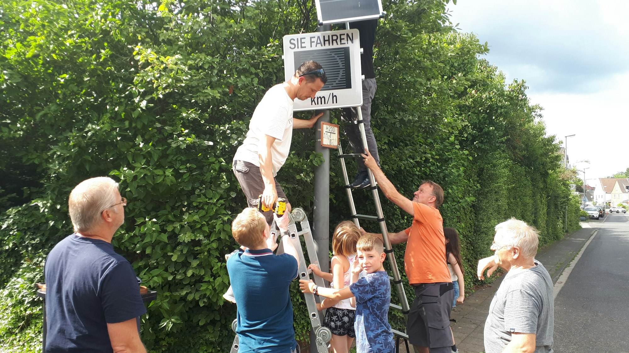 Männer und Kinder umringen eine Tempo-Messanlage. Zwei stehen auf Leitern.