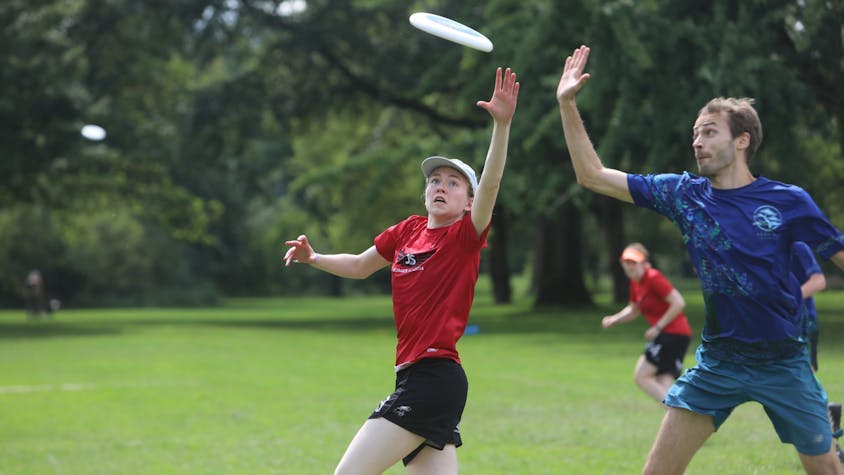 Eine Frau im roten Trikot und ein Mann im blauen Shirt versuchen, eine fliegende Frisbee-Scheibe zu fangen.