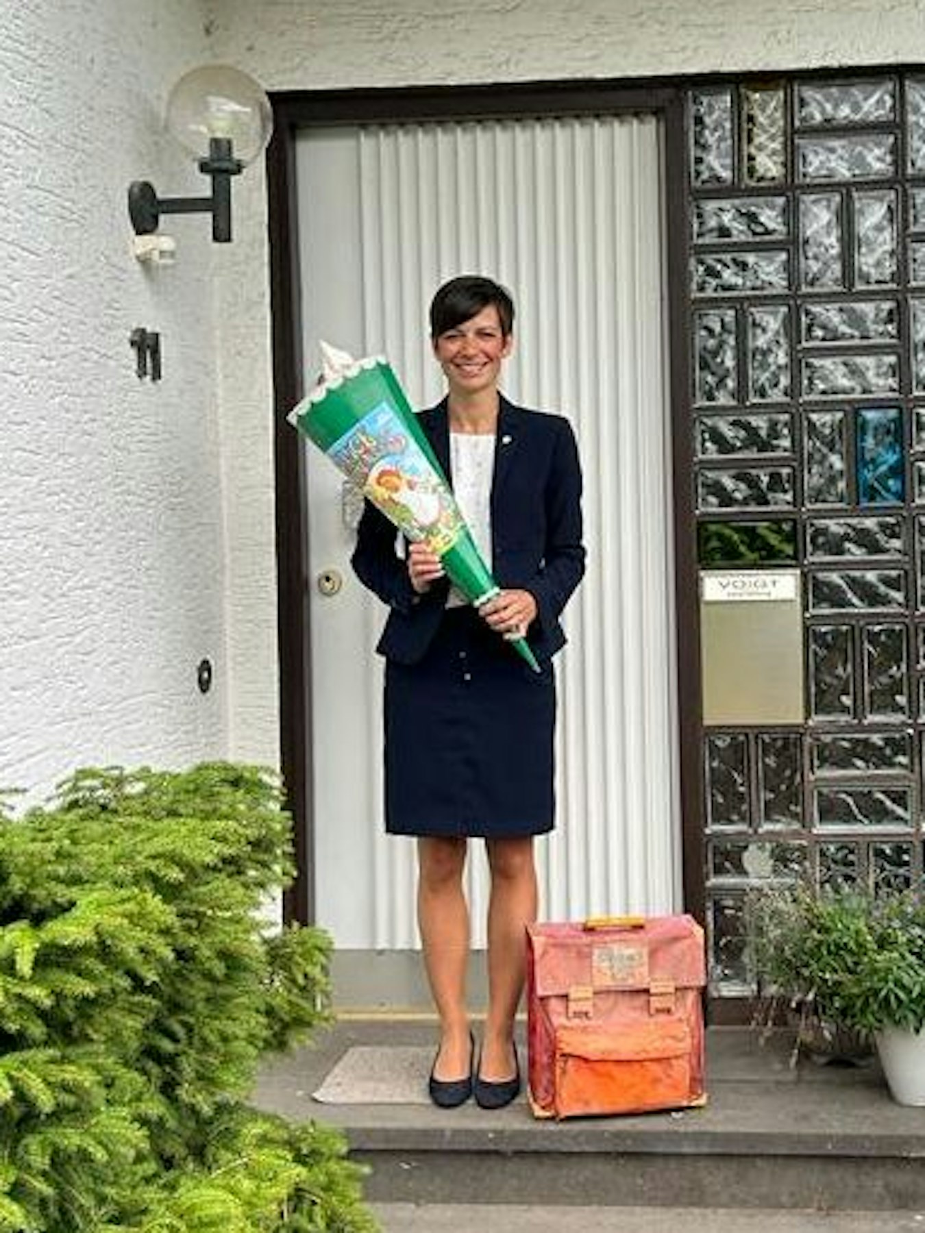 Das Bild zeigt die heutige Bürgermeisterin, Carolin Weitzel, vor ihrem Elternhaus. In der Hand hält sie ihre Schultüte.