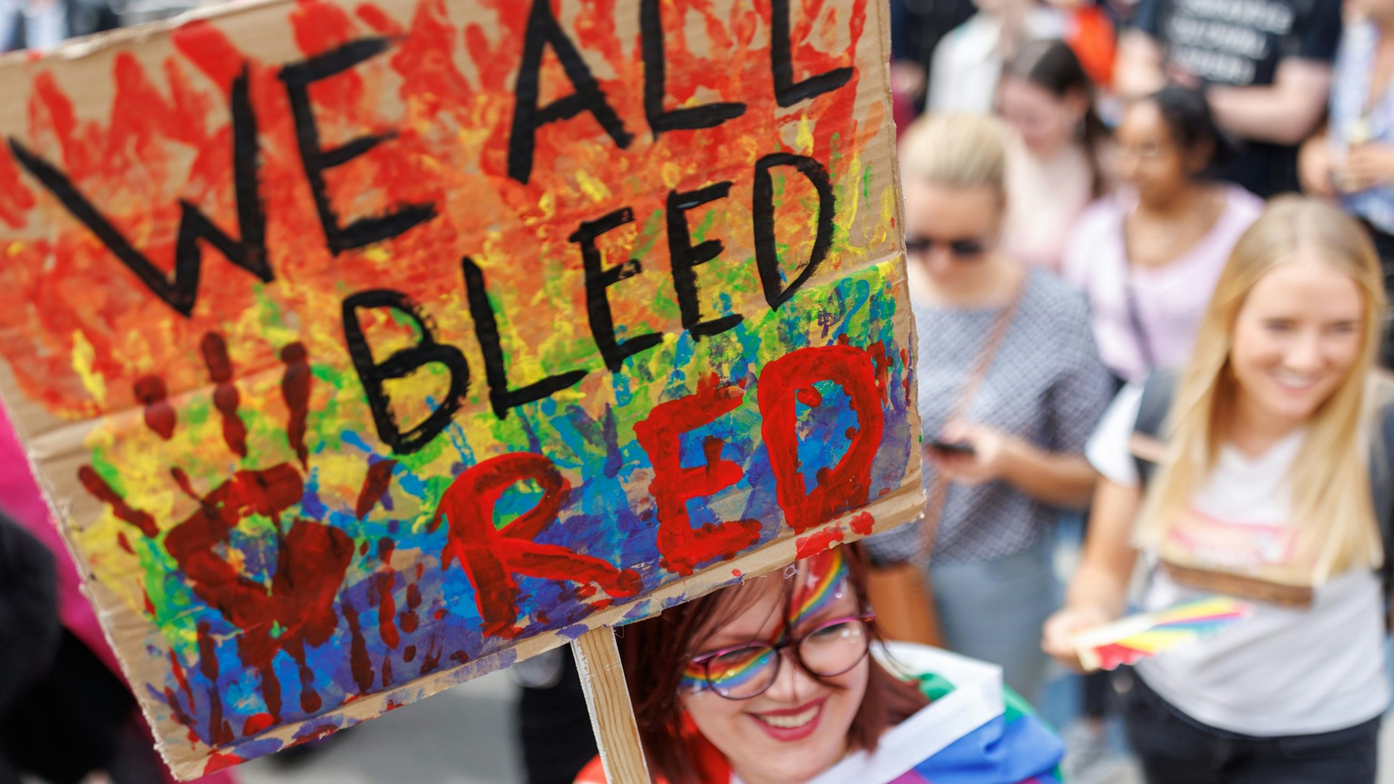 „We all bleed red“ steht auf dem Schild einer Teilnehmerin einer CSD-Demonstration im Rahmen der Nürnberger Prideweek.
