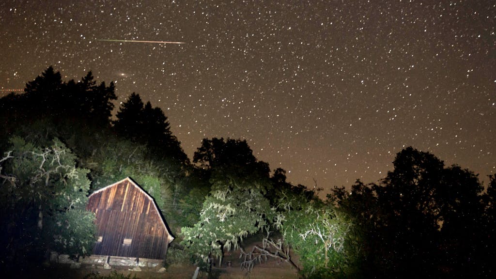Ein Meteor zieht am Himmel über einer Scheune vorbei.