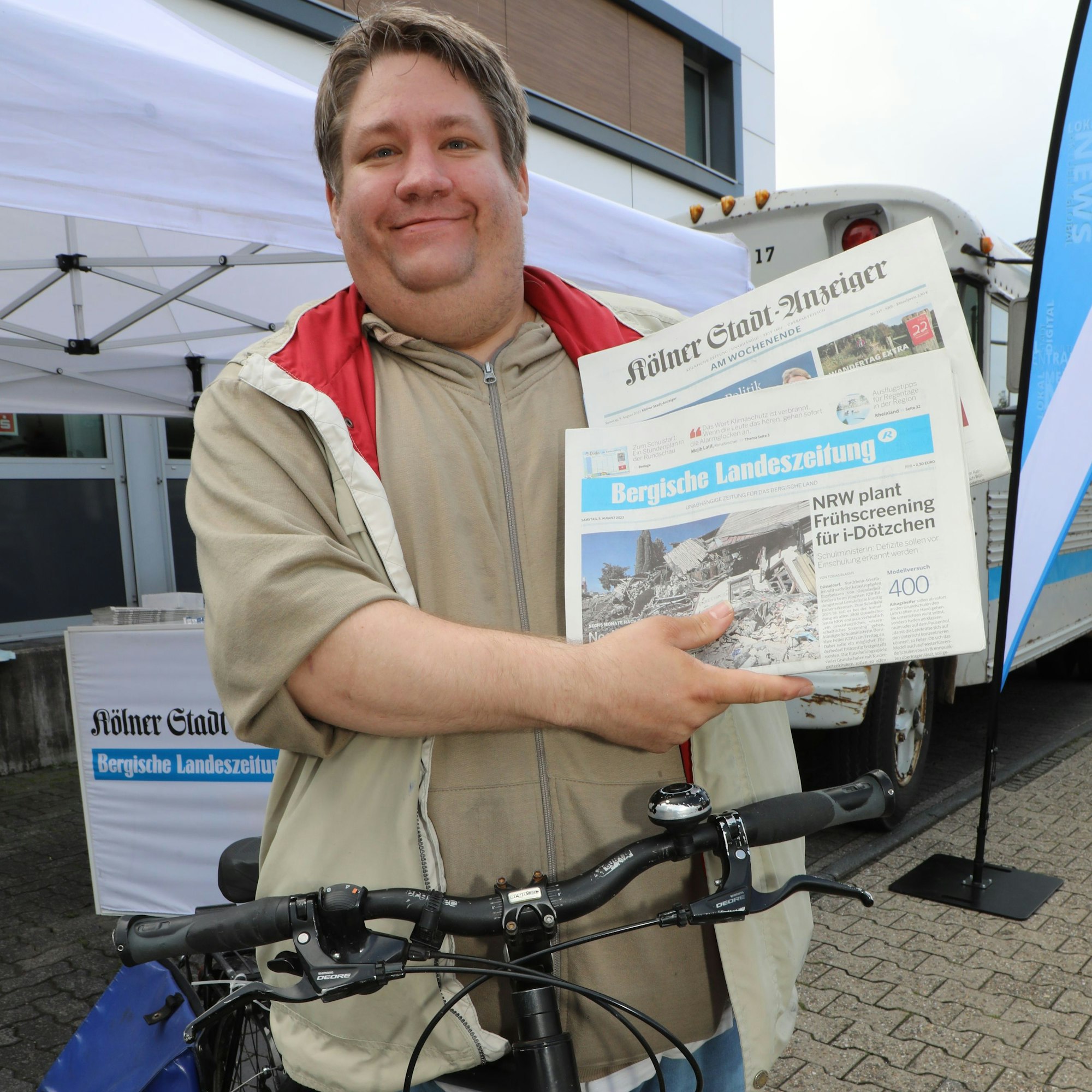 Zeitungszusteller Frank Schneider hält auf seinem Fahrrad eine Ausgabe der Bergischen Landeszeitung und eine des Kölner Stadt-Anzeiger in den Händen.
