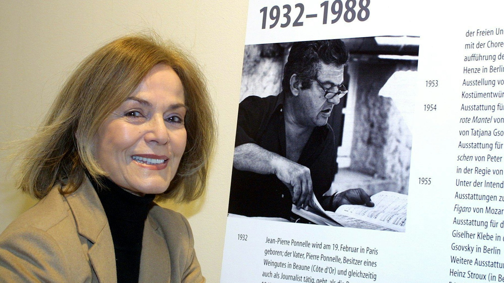 Margit Saad-Ponnelle, Schauspielerin und Regisseurin, steht neben einem Bild das ihren Ehemann, den Regisseur, Bühnen- und Kostümbildner Jean-Pierre Ponnelle, zeigt.