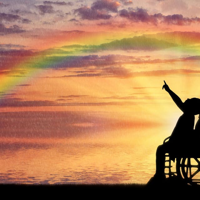 Die Silhouette eines Mädchens im Rollstuhl in der Abendsonne, das mit dem Finger auf einen Regenbogen zeigt.&nbsp;