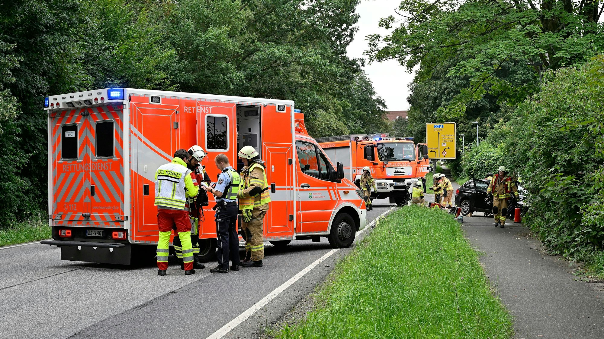 Ein Rettungswagen und ein Feuerwehrauto stehen auf einer Straße. Einsatzkräfte arbeiten an einem Autowrack.
