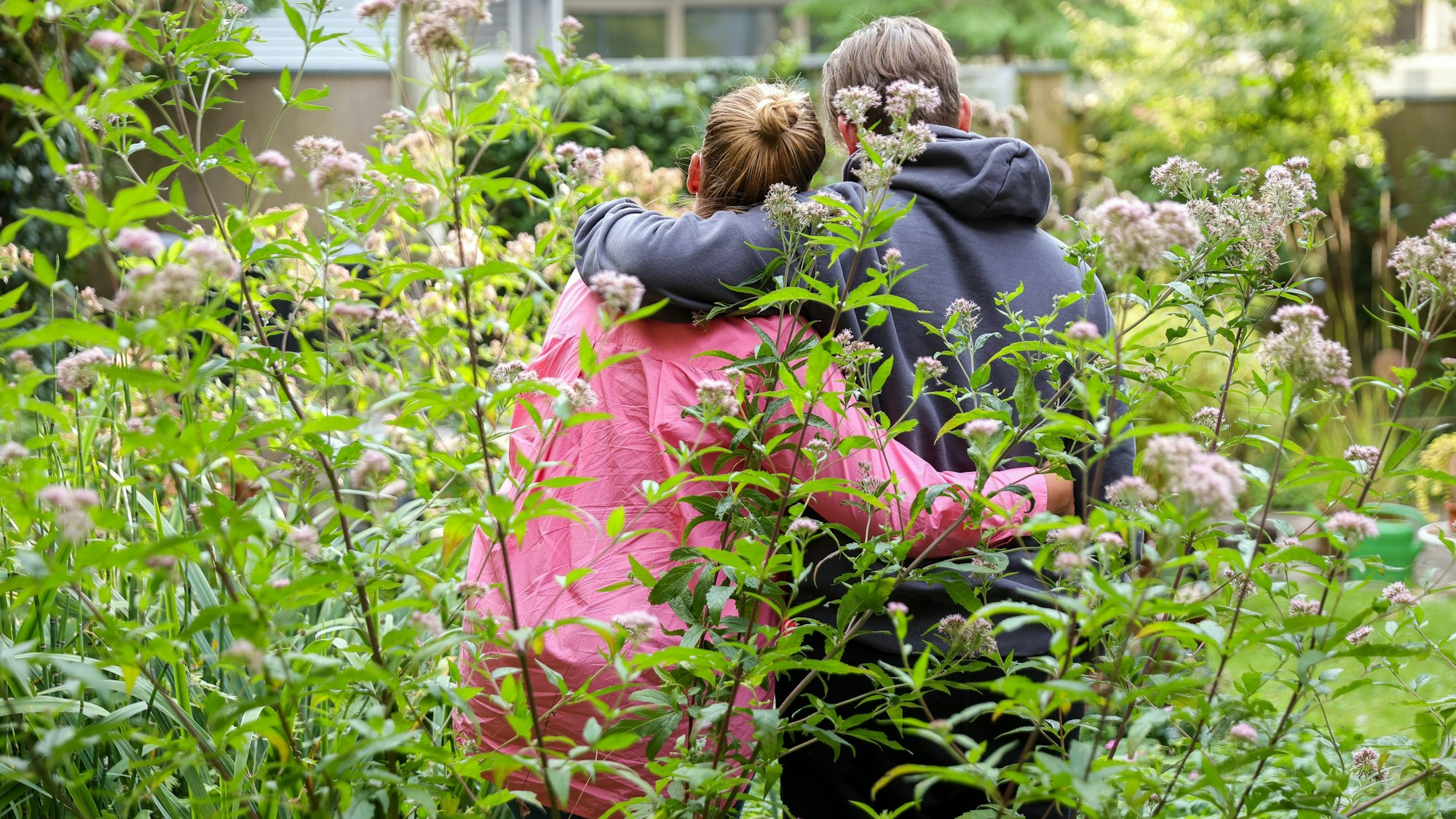 Svanja und Johann stehen in einem Garten, sie stehen mit dem Rücken zur Kamera und haben je einen Arm umeinander gelegt.