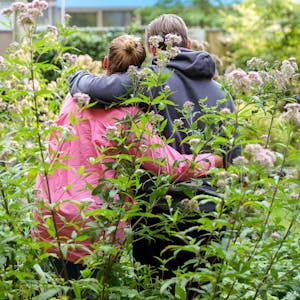 Svanja und Johann stehen in einem Garten, sie stehen mit dem Rücken zur Kamera und haben je einen Arm umeinander gelegt.&nbsp;