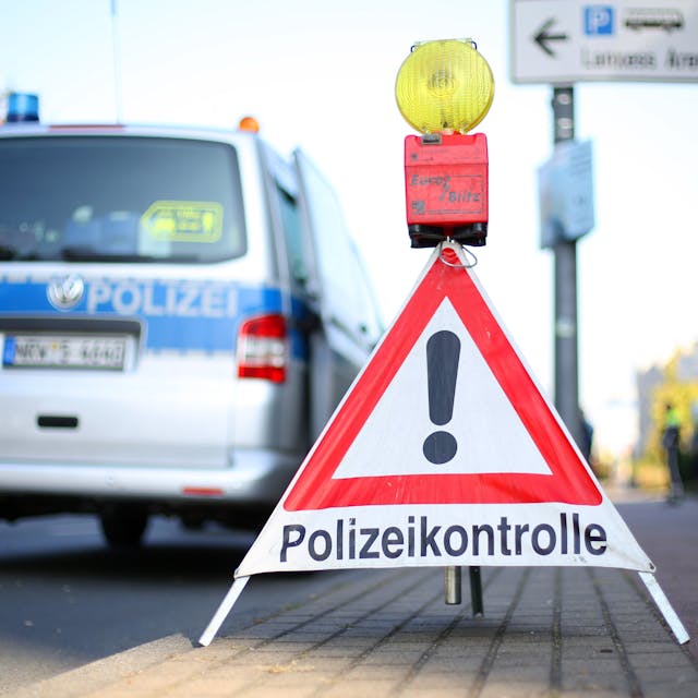 Ein Schild mit der Aufschrift Polizeikontrolle steht vor einem Einsatzwgen der Polizei