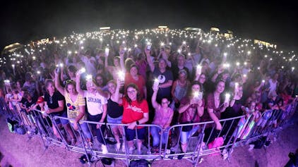 Hunderte Menschen stehen dicht gerdrängt vor einer Bühne, viele leuchten mit den Taschenlampen ihrer Handys.