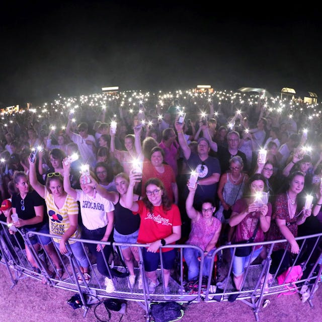 Hunderte Menschen stehen dicht gerdrängt vor einer Bühne, viele leuchten mit den Taschenlampen ihrer Handys.