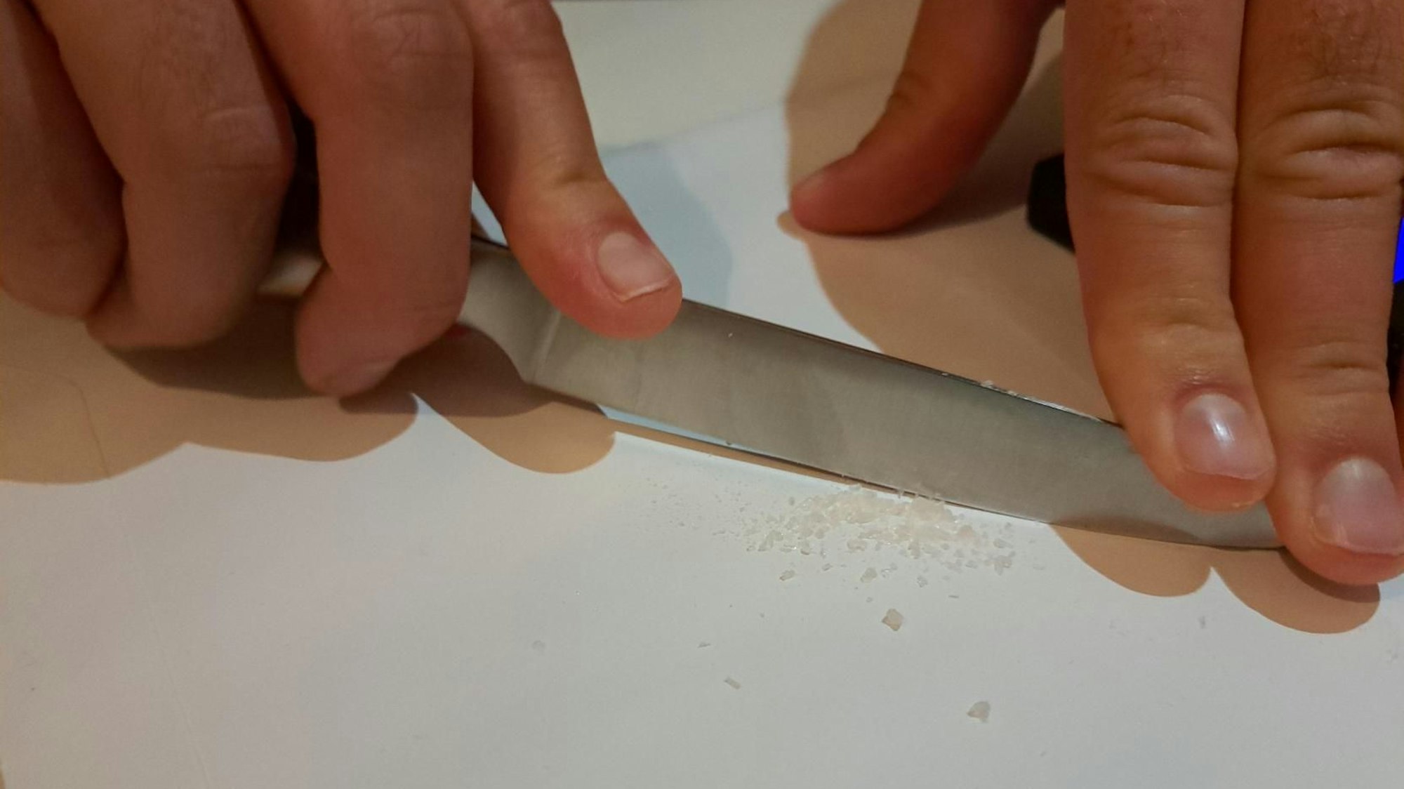 Hannes. S. zerkleinert die MDMA-Kristalle mit einem Küchenmesser.