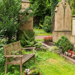 Eine Holzbank steht an einem Grab auf dem Melatenfriedhof.