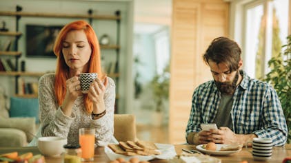 Mann und Frau beim Frühstück. Mann ist abgelenkt vom Smartphone.