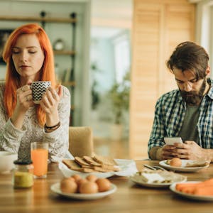 Mann und Frau beim Frühstück. Mann ist abgelenkt vom Smartphone.