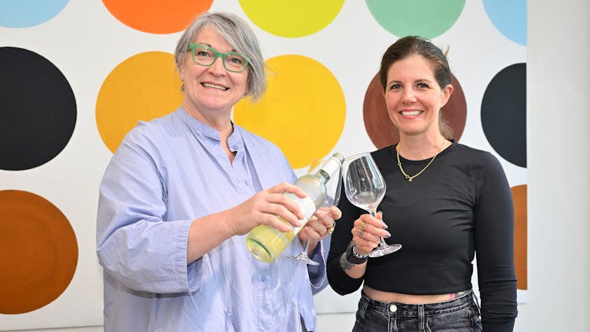 Dagmar Reitz und Katrin Gebauer vom Vorstand der IG Refrath stehen nebeneinander und gießen sich aus einer Weinflasche Wein ins Glas.&nbsp;