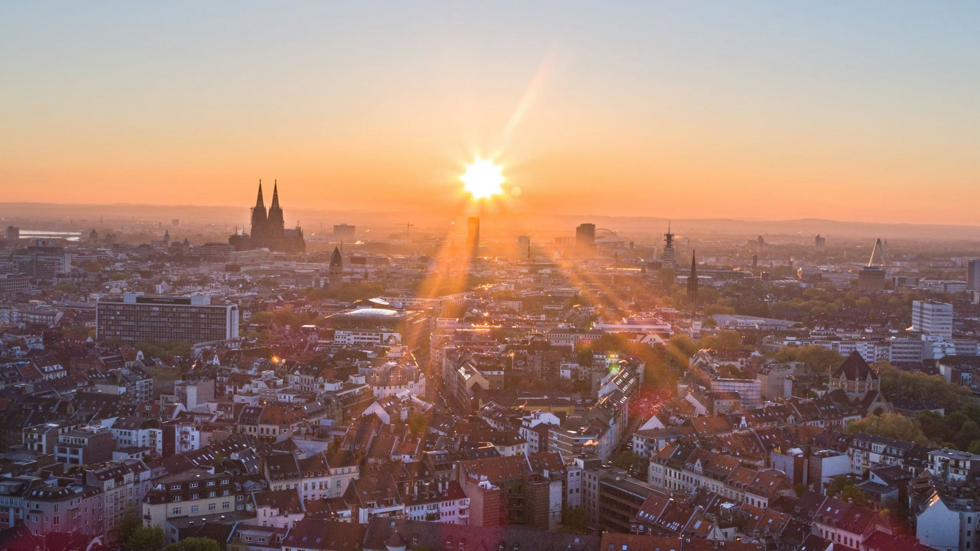 Die Sonne geht an einem wolkenlosen Morgen mit blauem Himmel neben dem Kölner Dom (Hohe Domkirche St. Petrus) über dem Stadtzentrum auf.