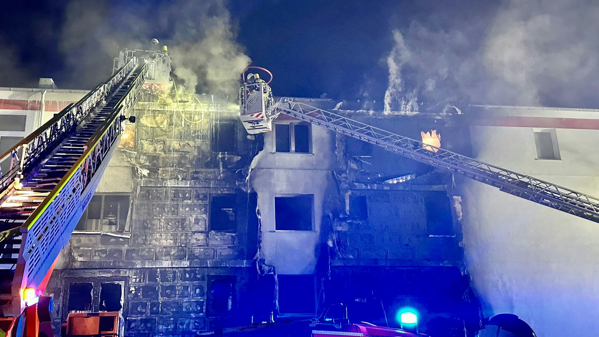 Über zwei Drehleitern löschen Feuerwehrleute eine brennende Hausfassade.