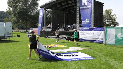 Helfer tragen Banner und Zaunelemente vor einer großen Bühne.