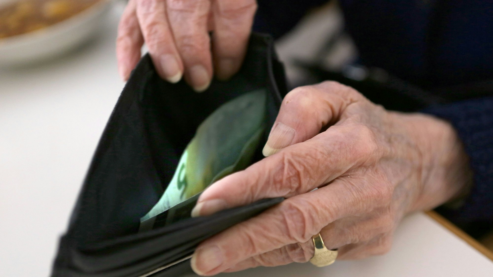 Das Symbolbild zum Thema Altersarmut zeigt die Hände einer alten Frau, die in ein Portemonnaie schaut, in dem sich ein Fünf-Euro-Schein befindet.