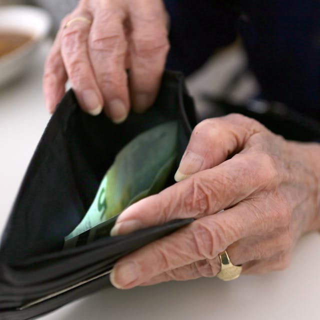 Das Symbolbild zum Thema Altersarmut zeigt die Hände einer alten Frau, die in ein Portemonnaie schaut, in dem sich ein Fünf-Euro-Schein befindet.