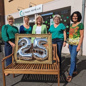 Vier Frauen stehen hinter einer Bank, auf der ein Rahmen mit der silbernen Zahl 25 platziert ist.